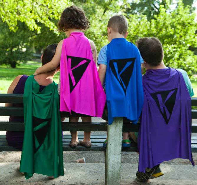 Family support during birth, family of four sitting on a park bench with backs to us, each one wears a cape