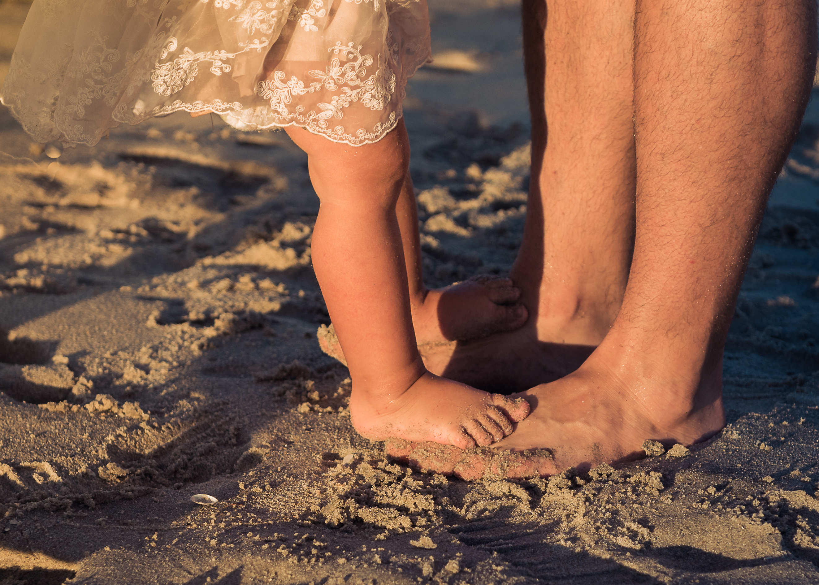 Close up of little girls feet stepping on her dad's feet at the beach - clients of Tribe of Mine