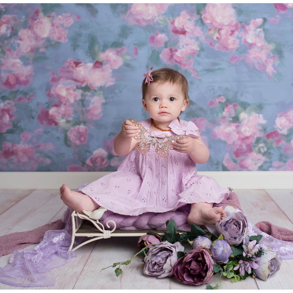 Little girl in purple dress sitting in front of purple flowered wall - Tribe of Mine.